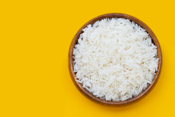 Wooden bowl of rice on yellow background.
