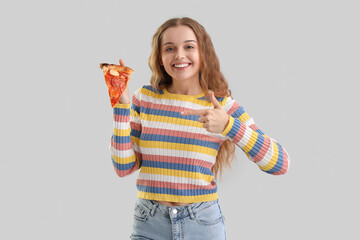Young woman with slice of tasty pizza showing thumb-up on grey background