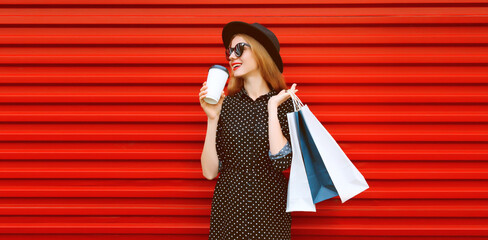 Portrait of happy smiling young woman with shopping bags wearing black round hat on red background