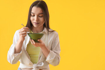 Young woman with spoon and bowl on yellow background