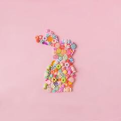 Plastic candies and flowers in the shape of a bunny against pink background. Minimal concept for Easter celebration banner or card. Flat lay.