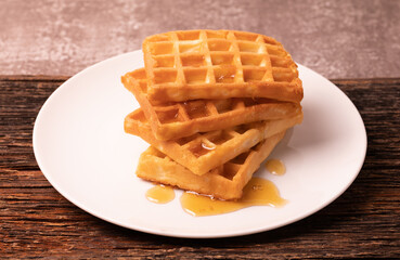 Delicious Belgian waffles with honey served on white plate and brown background, rustic concept.
