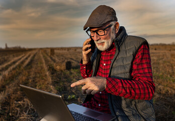 Happy farmer working on laptop in field