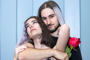 Portrait of young couple embracing and smiling at the camera. Couple in love holding a rose embracing and looking at the camera