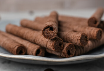 Plate of delicious rolled wafer cookies on grunge background, closeup