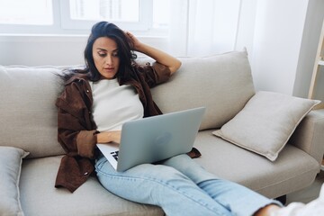 Obraz premium Woman freelancer on day off sitting on sofa with laptop at home online shopping on internet, smile