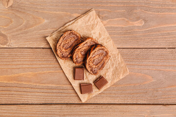 Baking paper with pieces of delicious sponge cake roll and chocolate on wooden table