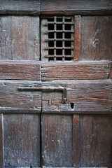 Old wooden door with iron grille and metal latch in Tuscany