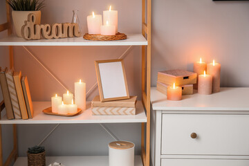 Interior of room with burning candles on drawer and shelving unit