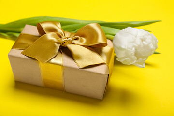 Beautiful gift and tulip flower for Women's Day celebration on yellow background, closeup