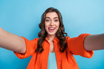 Photo of cheerful funny lady wear orange jacket recording self video sowing tongue isolated blue...