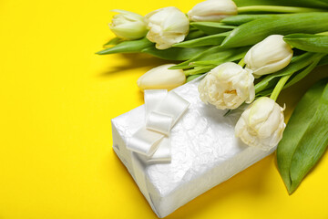Beautiful tulip flowers and gift for Women's Day celebration on yellow background, closeup