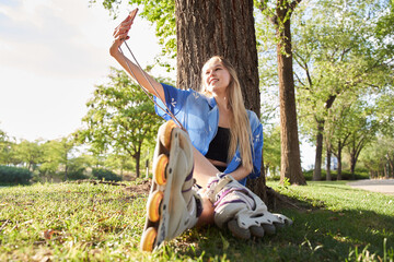 blonde woman sitting on a tree with inline skates on taking a selfie with her smart phone