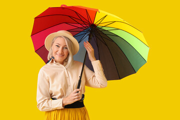 Beautiful mature woman with rainbow umbrella on yellow background