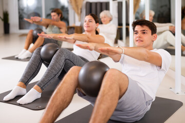 Fototapeta na wymiar Sporty energetic males and females doing exercises with pilates ball during group training at gym. Fitness concept.