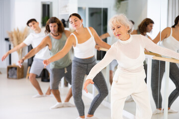 Gracile old-aged woman engaging in ballet at ballet barre in training hall during workout session