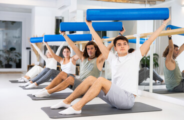Studious people doing pilates exercises with roller on gray mat during workout session