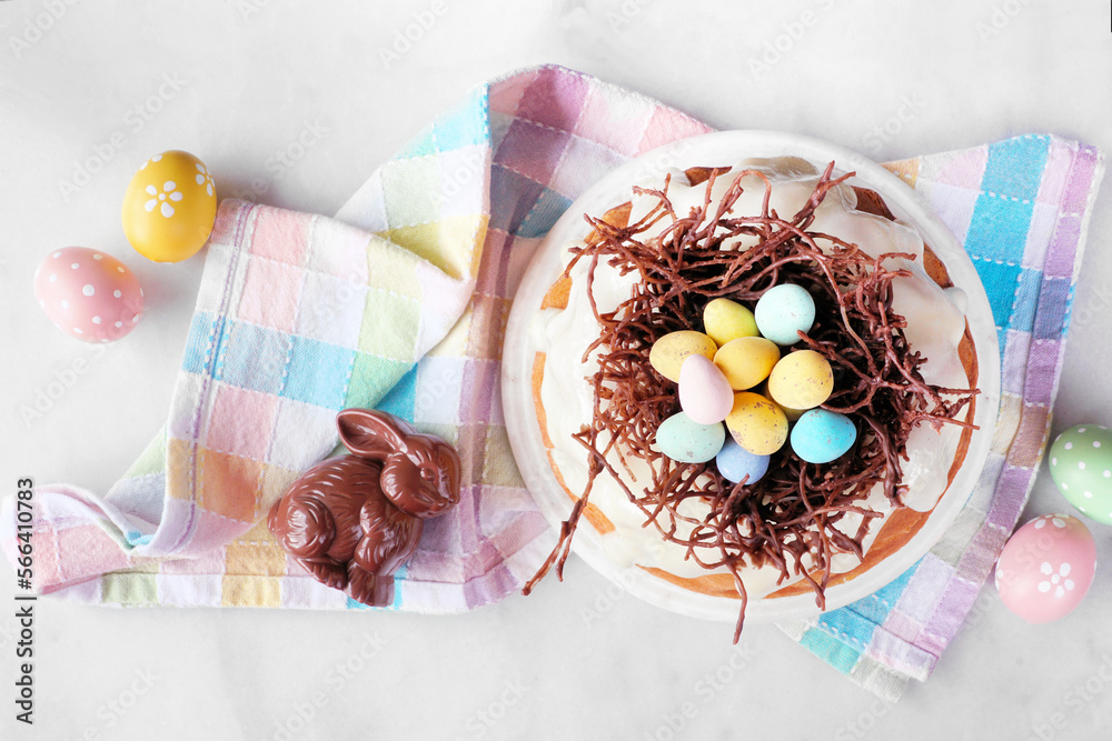 Poster easter bundt cake with chocolate nest of colorful candy eggs. top view table scene over a white ston