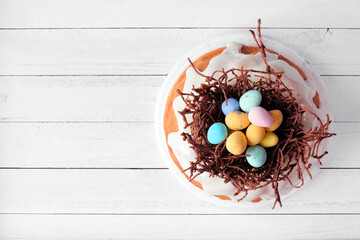 Easter bundt cake with chocolate nest of colorful candy eggs. Above view on a white wood background. - 566410757