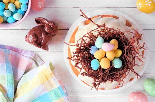 Easter bundt cake with chocolate nest of colorful candy eggs. Overhead view table scene on a white wood background.