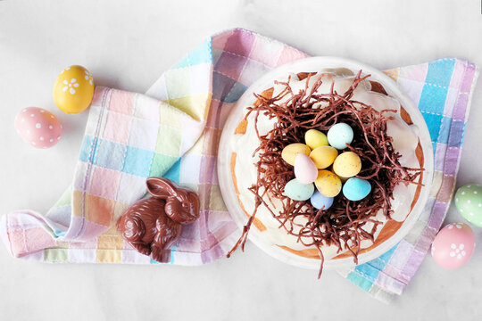 Easter bundt cake with chocolate nest of colorful candy eggs. Top view table scene over a white stone background.