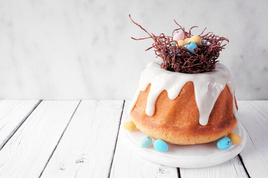 Easter bundt cake with chocolate nest of colorful candy eggs. Side view against a bright wood background.