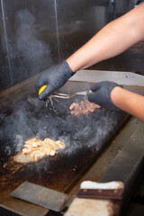 A view of hand squeezing a lemon onto chopped chicken breast, on a restaurant griddle surface.