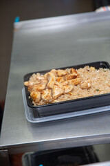 A view of a plastic to-go container filled with fried rice and grilled chopped chicken breast.
