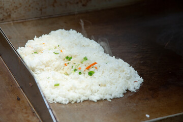 A view of a pile of fried rice on a restaurant griddle surface.