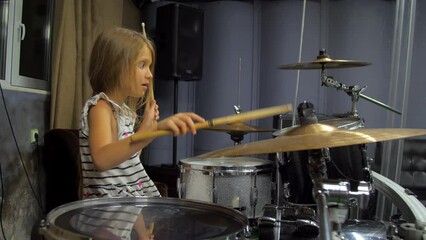 Junior schoolgirl learns playing drums hitting drums and cymbals with drumstick. Kid beats drumsticks against each other rhythmically
