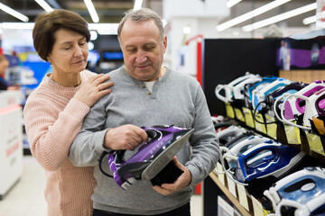 Senior couple choosing clothes iron while shopping in appliance store.