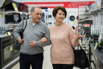 Fototapeta na wymiar Happy spouses of mature age, who came to the electronics and home appliances store, choose a gas stove to buy it