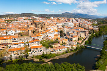 Fototapeta na wymiar View from drone of residential area of Plasencia city with brownish tiled roofs of houses and ancient gothic roman catholic cathedral on green bank of meandering Jerte river in spring, Caceres, Spain