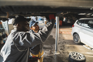 Obraz na płótnie Canvas Mechanics wearing gloves replacing a car's tyres on a lift in an auto repair shop. High-quality photo