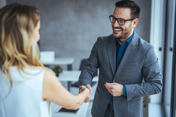 Business people shaking hands after successful meeting. Businessman And Businesswoman Shaking Hands In Office. Businessman shaking hands with his female partner celebrating successful teamwork. © Dragana Gordic