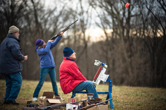 A woman shoots at two clay targets from a skeet machine.