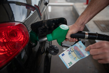 Hand of a man refueling the car and holding a 20€ banknote, concept of rising fuel prices.