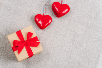 Two red toy hearts and gift box on fabric background. Valentines day concept. Top view, flat lay, copy space