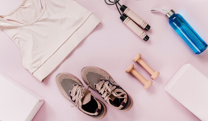 Set of accessories for fitness, yoga. Bra, pink block for yoga, bottle for water, dumbbells, sneakers, skipping rope on pink pastel background. Sports gear, minimalistic background. Close up
