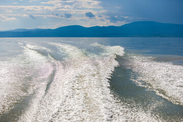 View of wake in water with mountain range in background.