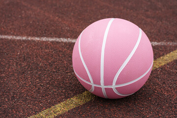 Pink basketball ball on the ground. Close-up ball on the red court. Basketball on the street or...