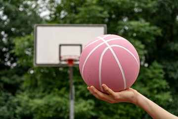 Pink basketball ball in man's hands in front of a basket outdoors. Minimal sport background. Sports gear, close up 