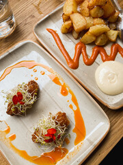 croquette tapas with microgreens and patatas bravas and a dipping sauce on a table in a cafe
