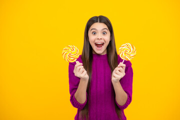 Excited face. Child eat lollipop popsicle over yellow isolated background. Yummy caramel, candy shop. Amazed expression, cheerful and glad.