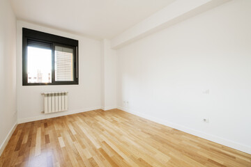 Empty living room with white walls, newly installed laminate flooring, black aluminum window with blind and radiator below