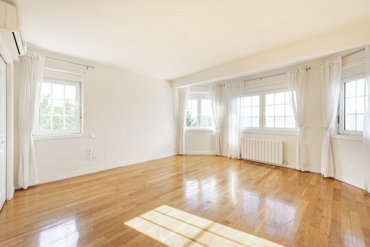 Empty living room with white semicircular walls, aluminum windows around the perimeter, white curtains fastened with ribbons and oak parquet floors