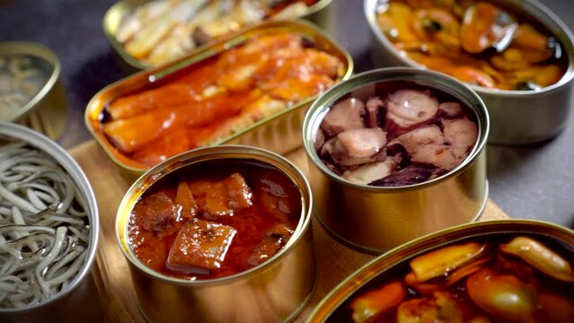 Preserve cans with different products, fish and seafood, natural or pickled, open on a dark table with a wooden cutting board and lemon. Ready to eat.