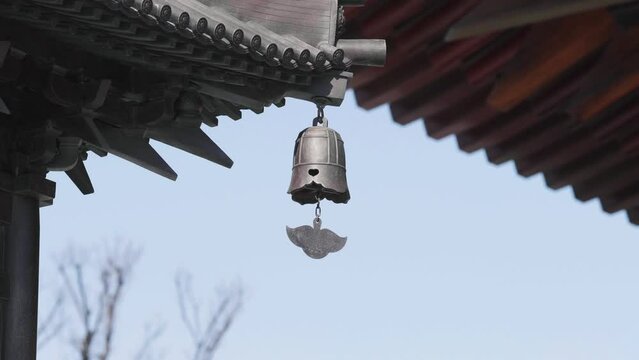 Close up of bronze bell swaying in wind with temple buildings background, 4k slow motion footage.