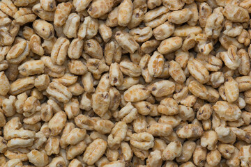 Dry honey puffed wheat cereal pieces scattered loosely directly above. Breakfast foods textured background, full frame image.