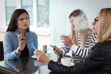 Women smoking cigarette at table in outdoor cafe - Powered by Adobe